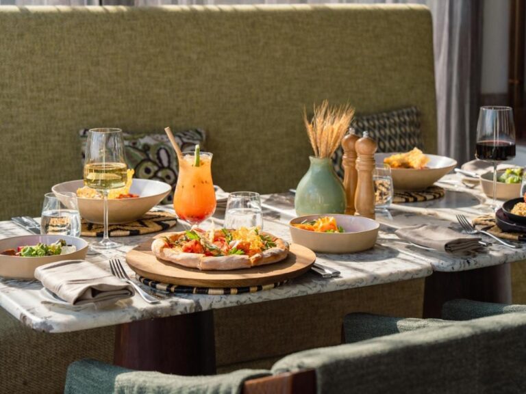 En pizza, salater, en cocktail og to vinglass på et marmorbord