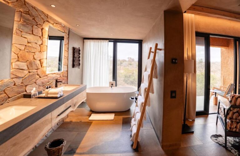 Badet i en suite, med badekar foran vinduet og dobbel vask mot en steinvegg