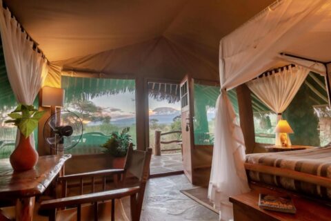 Et telt på Kibo Safari Camp som åpner seg mot terrassen, med Kilimanjaro i det fjerne i skumringen