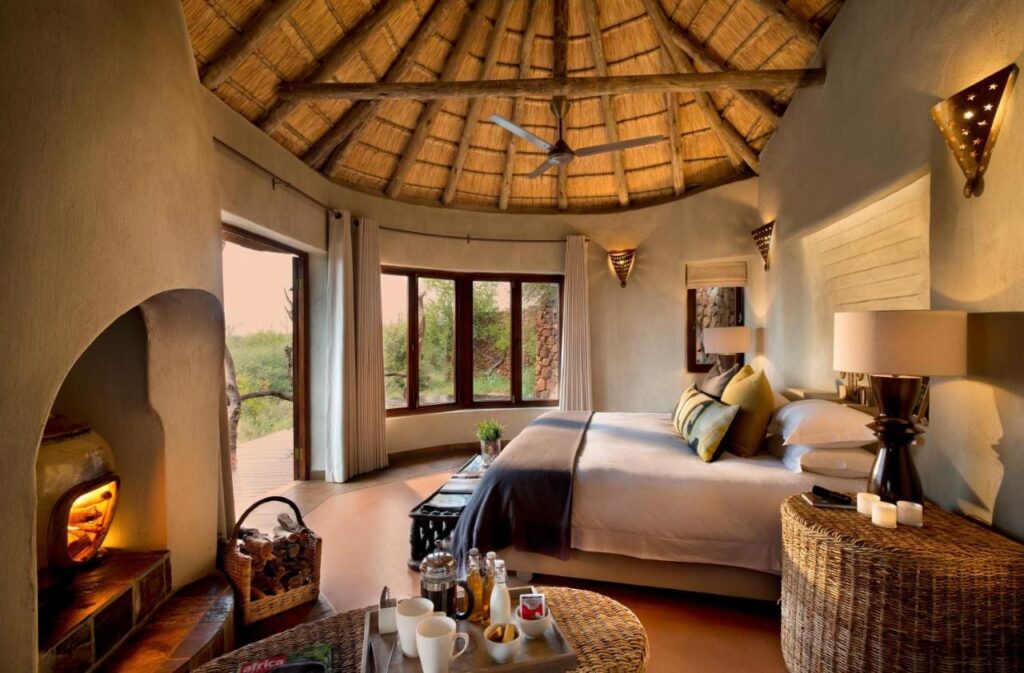 En suite på Madikwe Safari Lodge under et stråtak, med stor seng og fyr i peisen