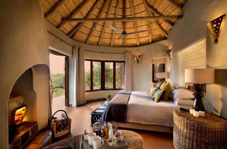 En suite på Madikwe Safari Lodge under et stråtak, med stor seng og fyr i peisen