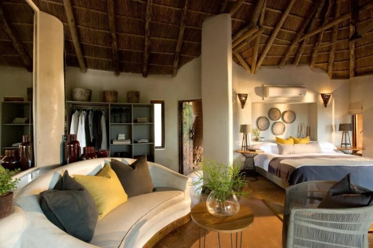 En suite på Madikwe Safari Lodge med en avrundet hvit sofa, stor seng og et åpent garderobeskap