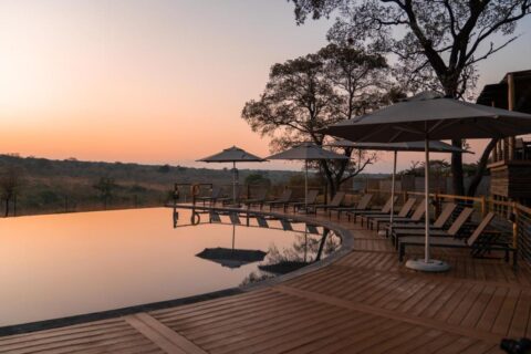 Uendelighetsbassenget på Mdluli Safari Lodge under en oransje himmel, omgitt av solsenger og parasoller
