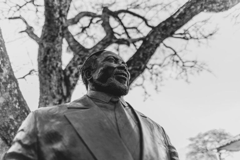 Bronsestatuen av en smilende mann med skjegg, i dress, under et tre, i svart-hvitt