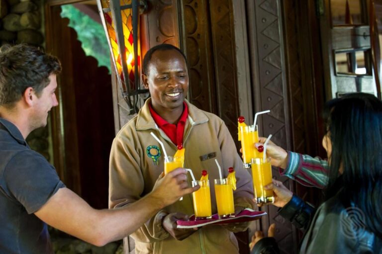 En ansatt på Ngorongoro Serena Safari Lodge rekker fram et brett med fruktjuice til to reisende