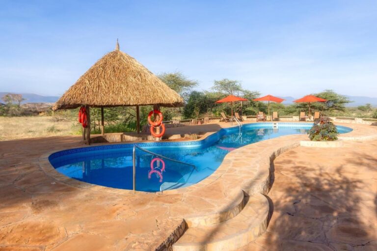 Bassenget på Samburu Sopa Lodge, med stråhytta med oransje livbøyer og røde parasoller mot bushen