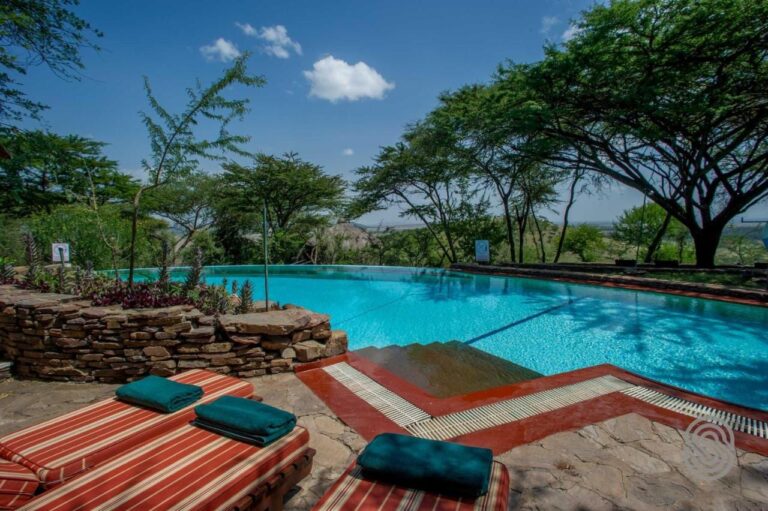Uendelighetsbassenget på Serengeti Serena Safari Lodge, med rødstripete solsenger og grønne håndklær, under akasiene