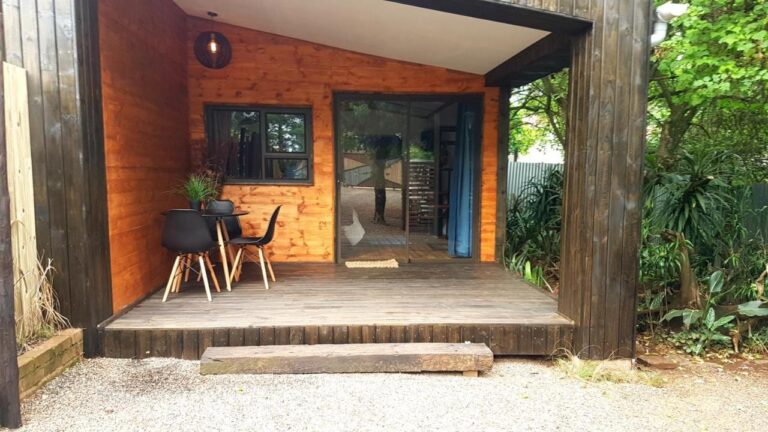 Treterrassen til en hytte, med et bord og to svarte stoler foran en skyvedør i glass