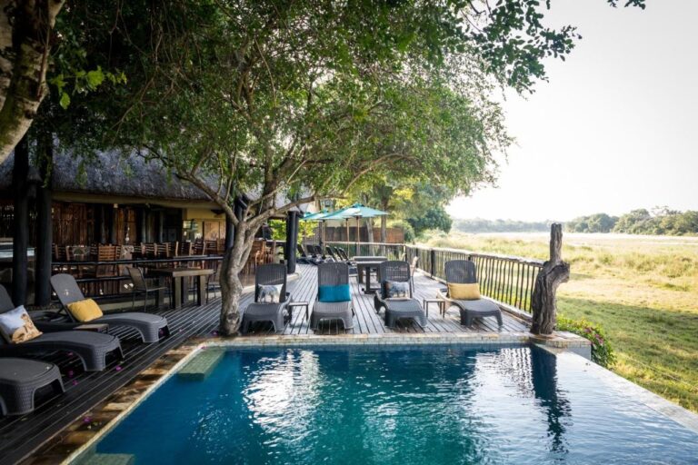 Bassenget på Umkumbe Safari Lodge og treterrassen, over den gressgrodde elvebredden