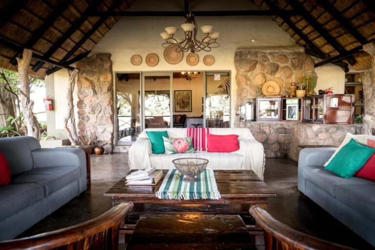 Den åpne salongen på Umkumbe Safari Lodge, under stråtaket, med grå sofaer og steinvegger